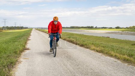 Photo for Senior athletic man is riding a gravel touring bike - biking on a levee trail along Chain of Rocks Canal near Granite City in Illinois - Royalty Free Image
