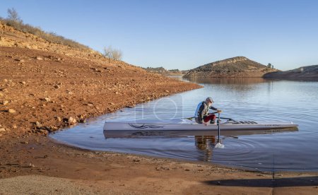 Photo for Fort Collins, CO, USA - December 6, 2023: Senior man in a coastal rowing shell, Literace 1x by Litebox, on a shore of Horsetooth Reservoir in fall or winter scenery. - Royalty Free Image