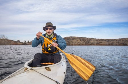 Téléchargez les photos : Senior male in life jacket is paddling expedition canoe, décor de la saison froide sur Horsetooth Reservoir dans le nord du Colorado, Point de vue de la caméra d'action - en image libre de droit