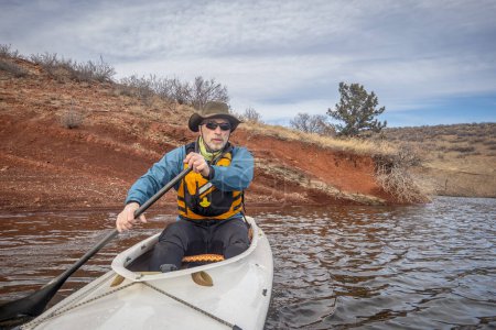 Foto de Senior macho en chaleco salvavidas es remar canoa expedición, paisaje de temporada fría en el embalse de dientes de caballo en el norte de Colorado, POV de cámara de acción - Imagen libre de derechos
