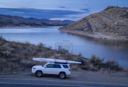 Foto de Fort Collins, CO, Estados Unidos - 19 de diciembre de 2023: Toyota 4runner SUV with a rewing shell, LiteRace 1x by Liteboat on roof racks on a shore of Horsetooth Reservoir - fall or winter dusk scenery. - Imagen libre de derechos