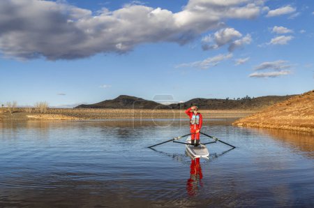 Photo for Senior male rower is standing in a coastal rowing shell - Horsetooth Reservoir in fall or winter scenery in northern Colorado. - Royalty Free Image
