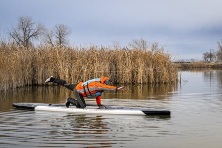 Photo for Senior male stand up paddler is practicing yoga poses on his paddleboard on a lake in Colorado, winter or fall scenery - Royalty Free Image