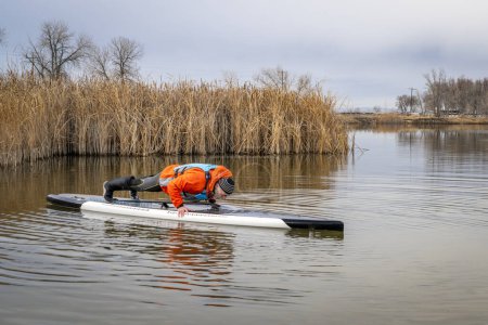 Photo for Senior male stand up paddler is practicing push ups on his paddleboard on a lake in Colorado, winter or fall scenery - Royalty Free Image