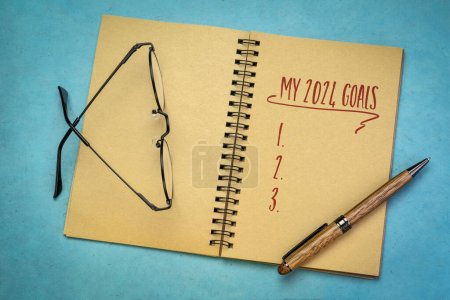 Foto de Mi lista de objetivos 2024 en un cuaderno con bolígrafo y gafas de lectura, estableciendo metas y resoluciones de Año Nuevo - Imagen libre de derechos