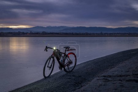 Foto de Bicicleta de grava en una orilla de un lago congelado con vista lejana de las Montañas Rocosas, atardecer de invierno en el norte de Colorado - Imagen libre de derechos