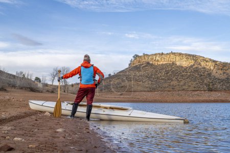 Téléchargez les photos : Pagayeur mâle avec un canot d'expédition ponté et une pagaie en bois sur une rive du réservoir Horsetooth dans le nord du Colorado dans des paysages de saison froide - en image libre de droit
