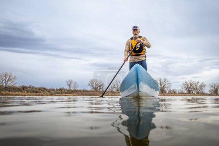 Photo for Senior male paddler is paddling a stand up paddleboard on a calm lake in spring, frog perspective from an action camera at water level - Royalty Free Image