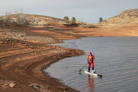 Photo for Winter stand up paddling in Colorado - male paddler in a drysuit on Horsetooth Reservoir - Royalty Free Image