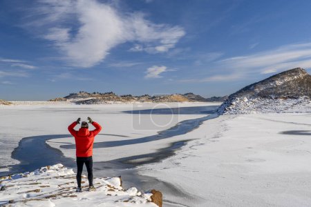 Téléchargez les photos : Randonneur masculin en doudoune sur une rive rocheuse du réservoir Horsetooth gelé dans le nord du Colorado - en image libre de droit