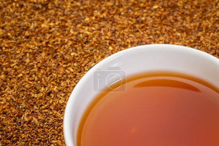Photo for Rooibos red tea  -  a white cup of a hot drink and loose leaves on grunge wood background, tea made from the South African red bush, naturally caffeine free - Royalty Free Image