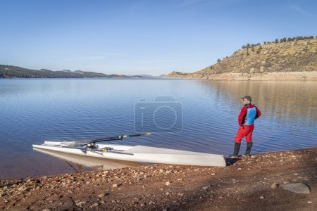 Photo for Senior male rower and a coastal rowing shell is landing on a rocky shore of Carter Lake in fall or winter scenery in northern Colorado. - Royalty Free Image
