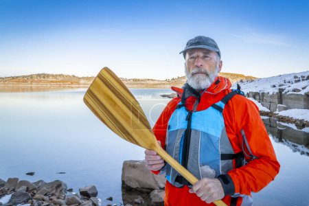 Téléchargez les photos : Pagayeur de canot senior portant un gilet de sauvetage sur une rive du lac Carter dans le nord du Colorado dans des paysages d'hiver - en image libre de droit