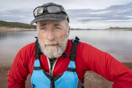 Téléchargez les photos : Portrait environnemental d'un pagayeur de sexe masculin portant une combinaison sèche et un gilet de sauvetage sur la rive d'un lac au Colorado en hiver - en image libre de droit