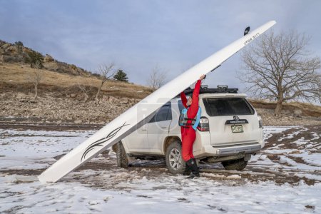 Téléchargez les photos : Loveland, CO, États-Unis - 6 février 2024 : Un rameur sénior charge une coque d'aviron Liteboat sur les supports de toit du VUS Toyota 4Runner sur une rive du lac Carter, dans le nord du Colorado, dans un paysage hivernal. - en image libre de droit