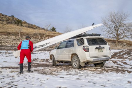 Téléchargez les photos : Loveland, CO, États-Unis - 6 février 2024 : Un rameur sénior charge une coque d'aviron Liteboat sur les supports de toit du VUS Toyota 4Runner sur une rive du lac Carter, dans le nord du Colorado, dans un paysage hivernal. - en image libre de droit