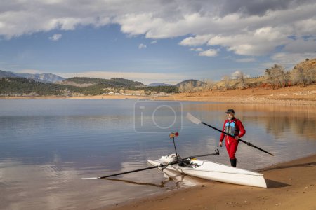 Téléchargez les photos : Rameur senior est gréer sa coquille d'aviron sur une rive du lac Carter dans le nord du Colorado dans les paysages d'hiver - en image libre de droit