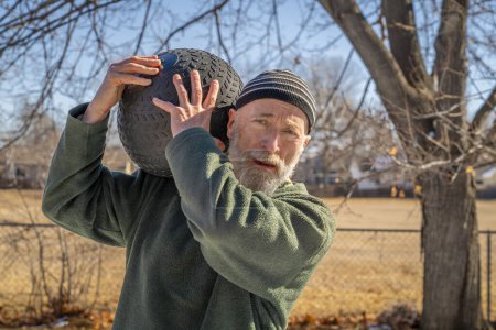Téléchargez les photos : Senior homme est l'exercice avec un lourd, 50 lb, boule de claquement dans son arrière-cour, journée ensoleillée d'hiver - en image libre de droit