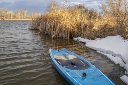 Photo for Touring stand up paddleboard with a safety leash on a shore of lake in northern Colorado, winter or early spring scenery with some snow - Royalty Free Image
