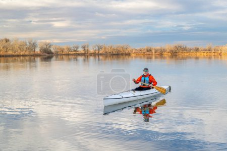 Photo for Senior male paddler is paddling a decked expedition canoe on a calm lake in northern Colorado, winter scenery without snow - Royalty Free Image