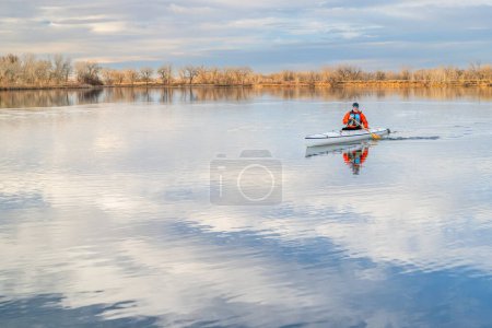 Téléchargez les photos : Senior mâle pagayeur pagaie un canot d'expédition ponté sur un lac calme dans le nord du Colorado, décor d'hiver sans neige - en image libre de droit