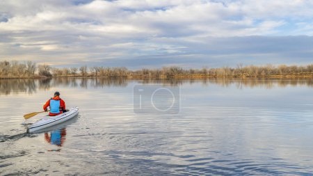 Téléchargez les photos : Senior mâle pagayeur pagaie un canot d'expédition ponté sur un lac calme dans le nord du Colorado, décor d'hiver sans neige - en image libre de droit