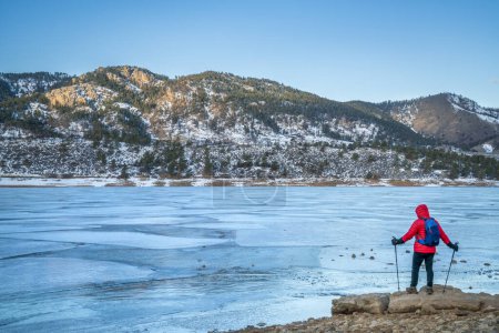 männliche Wanderer mit Trekkingstöcken am Ufer des gefrorenen Horsetooth Reservoir in der Nähe von Fort Collins, Colorado - Winterwanderkonzept