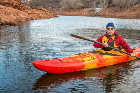 senior male paddler is paddling colorful river kayak on a calm lake  - recreation concept, cold season on Horsetooth Reservoir in Colorado