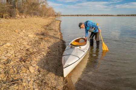 Téléchargez les photos : Pagayeur mâle senior avec canot ponté d'expédition sur une rive du lac au début du printemps, réservoir Boedecker dans le nord du Colorado - en image libre de droit