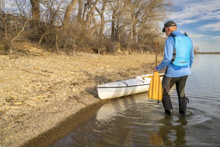 remo macho senior con canoa cubierta de expedición en una orilla del lago a principios de primavera, embalse Boedecker en el norte de Colorado