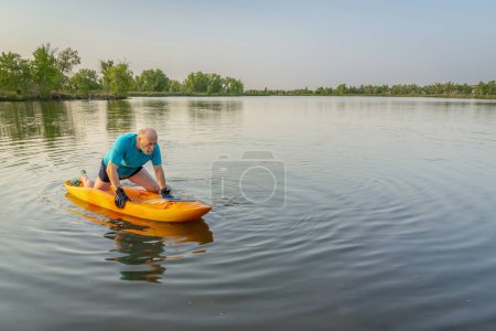 Photo for Athletic, senior man is paddling a prone kayak on a lake in Colorado, this water sport combines aspects of kayaking and swimming - Royalty Free Image