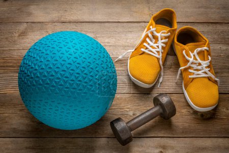 Photo for Heavy rubber slam ball filled with sand, iron dumbbell and minimalist barefoot sneakers on a rustic wooden deck, exercise and fitness concept - Royalty Free Image