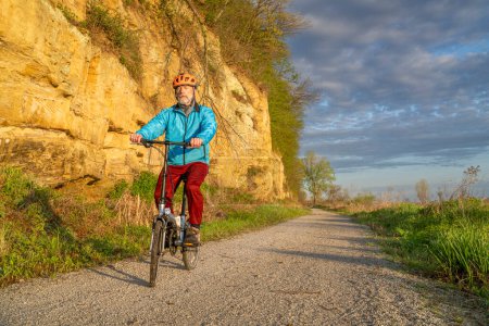 Photo for Male cyclist riding a folding bike on Steamboat Trace, bike trail converted from an abandoned railroad, near Peru, Nebraska, springtime morning scenery - Royalty Free Image