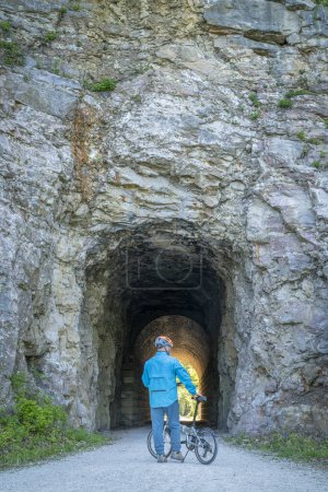 Téléchargez les photos : Homme cycliste avec un vélo pliant sur Katy Trail dans un tunnel près de Rocheport, Missouri, paysage printanier. Le sentier Katy est un sentier cyclable de 237 milles converti d'un ancien chemin de fer. - en image libre de droit
