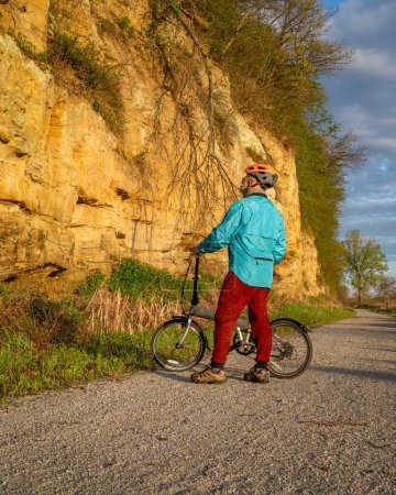 Photo for Senior male cyclist with a folding bike on Steamboat Trace, bike trail converted from an abandoned railroad, near Peru, Nebraska, springtime morning scenery - Royalty Free Image