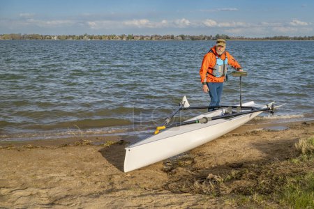Senior male rower with his rowing shell on a beach of Boyd Lake in northern Colorado, serly spring scenery