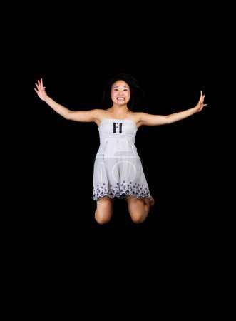 Photo for Young Japanese Woman With Big Clenched Teeth Expression Jumping In Whte Dress Against Black Background - Royalty Free Image