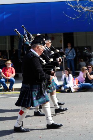Photo for Men Marching In Parade Playing Bagpipes Wearing Kilts With Spectators In Background Yuba City California - Royalty Free Image