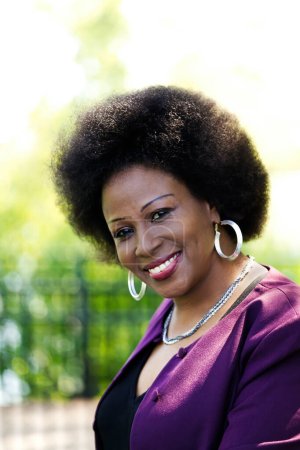 Foto de Mujer afroamericana mayor al aire libre retrato sonriente con chaqueta púrpura y top negro - Imagen libre de derechos