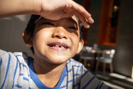 Asiatischer kleiner Junge lächelt und zeigt, dass ihm gerade sein Milchzahn gezogen wurde