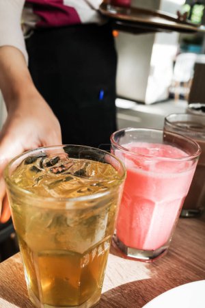 Tee und rosa Erdbeermilchgetränke, die von der Kellnerin in einem Restaurant in Gläsern serviert werden