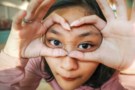 Photo for Asian teen girl making gesture with her hands on her face as if using eyeglasses - Royalty Free Image