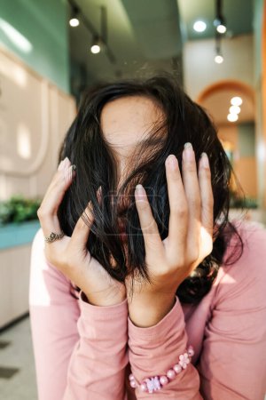 Asiatisches Teenager-Mädchen stützt ihr Kinn auf ihre Hände und bedeckt ihr Gesicht mit ihren Haaren