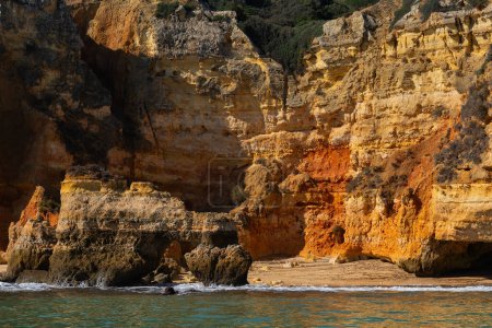 Secluded hidden beach below scenic cliffs as seen from the ocean side in Lagos, Algarve region, Faro District, Portugal.