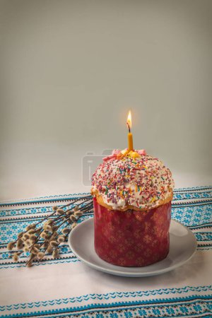 Photo for Traditional Kulich with  icing and willow twigs. Palm Sunday. Burning candle on an Easter cake is a symbol of the spiritual light of Jesus. Mass produced products - Royalty Free Image