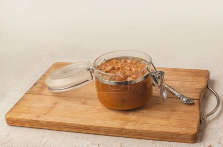 Téléchargez les photos : Pot ouvert de chutney de pommes, tomates, oignons et épices sur une planche à découper sur une table. - en image libre de droit