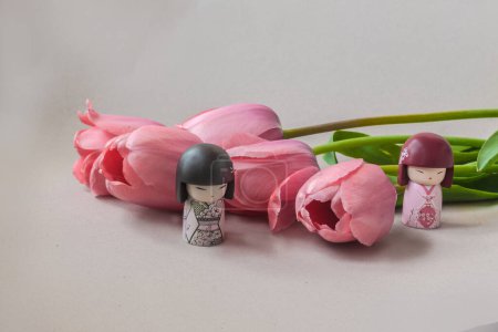 Foto de Ramo de cinco tulipanes rosados y muñecas japonesas kokeshi (producción en masa) sobre fondo gris. Concepto de hanami, admirando y contemplando la belleza de la naturaleza. Lugar para el texto. - Imagen libre de derechos