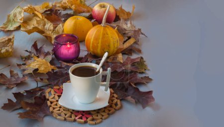 Cup of coffee on a wooden table with fallen leaves, burning candle and pumpkins. Background for calendar, postcard, flyer, banner. Place for text