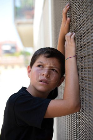 Foto de Niño en pantalones cortos y camiseta negra apoyado en una pared mientras mira hacia otro lado - Imagen libre de derechos