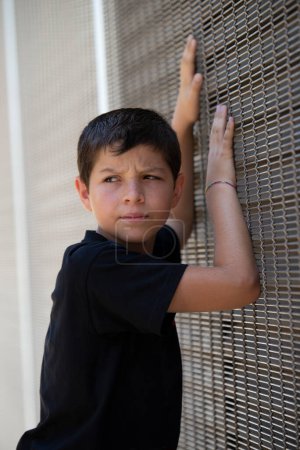 Foto de Niño en pantalones cortos y camiseta negra apoyado en una pared mientras mira hacia otro lado - Imagen libre de derechos